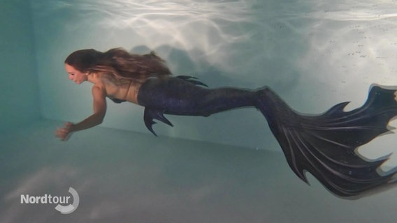 Unterwasseraufnahme von einer Frau, die als Meerjungfrau durch das Wasser schwimmt. © Screenshot 