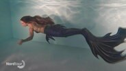 Unterwasseraufnahme von einer Frau, die als Meerjungfrau durch das Wasser schwimmt. © Screenshot 