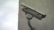 Eine Überwachungskamera an einer grau verputzten Außenwand. © Screenshot 