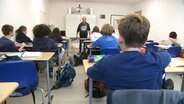 Ein Klassenzimmer mit Schülern und einem Lehrer. © Screenshot 