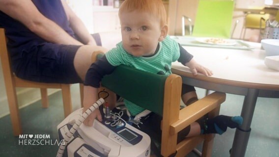 Ein Kleinkind sitzt auf einem Stuhl, hinter dem ein großes medizinisches Gerät steht. © Screenshot 