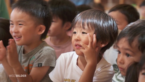 Viele japanische Kinder sitzen in Reihen und lauschen aufmerksam und interessiert einem Vortrag. © Screenshot 