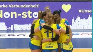Die Volleyballerinnen des SSC Palmberg Schwerin stehen bei einem Spiel in einem engen Kreis mit um die Schultern gelegten Armen. © Screenshot 