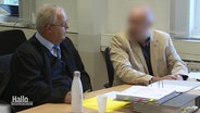 Ein Angeklagter mit verpixeltem Gesicht bespricht sich vor Gericht mit seinem Anwalt. © Screenshot 