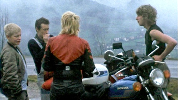 Filmstill 70er-Jahre. Drei Jugendliche und ein Erzieher stehen an zwei Motorrädern neben einer Landstraße. © NDR Dokfilm 