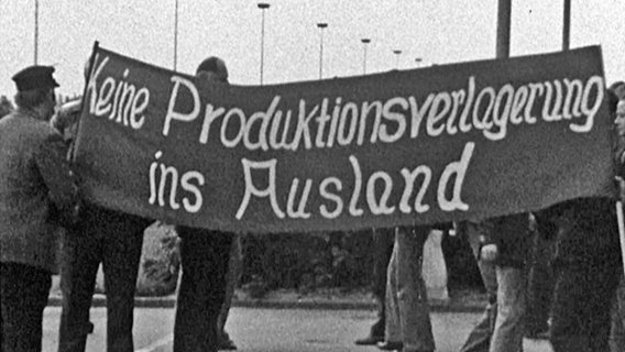 Historisches Bild einer Demonstration von VW-Arbeitern mit einem Transparent und der Aufschrift: keine Produktionsverlagerung ins Ausland. © Screenshot 