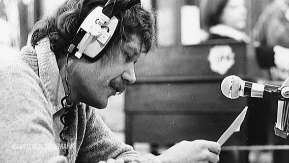 Schwarz-Weiß-Aufnahme: Carlo von Tiedemann mit Kopfhörern an einem Mikrofon © Screenshot 