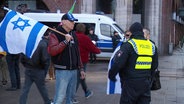 Ein Mann mit einer israelischen Flagge und ein Polizist in einer Warnweste. © Screenshot 