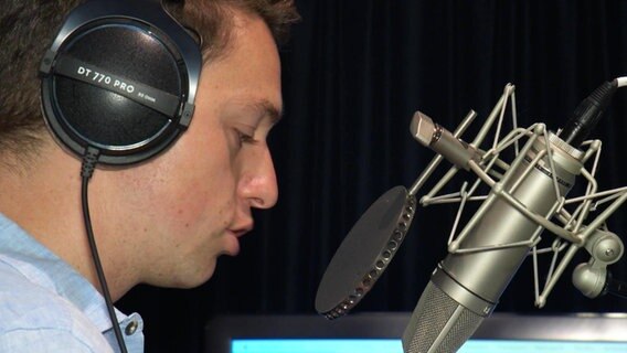 Ein Mann spricht in ein Mikrofon. © Screenshot 