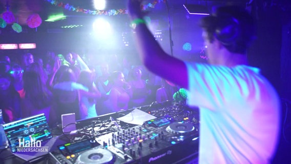 Die Sicht von einem DJ-Pult aus in einen bunt erleuchteten Club mit tanzenden Menschen. © Screenshot 