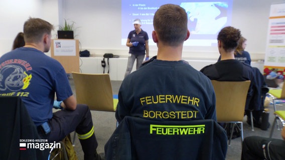 Menschen auf Stühlen in T-Shirts auf denen Feuerwehr Borgstedt steht. © Screenshot 