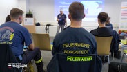 Menschen auf Stühlen in T-Shirts auf denen Feuerwehr Borgstedt steht. © Screenshot 