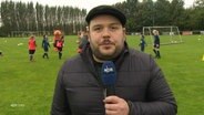 NDR-Reporter Jan Bockemüller steht am Rand eines Fußballfeldes. © Screenshot 