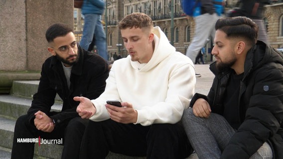 Nikodem Kaddoura und zwei andere Männer sitzen auf einer Treppe. © Screenshot 
