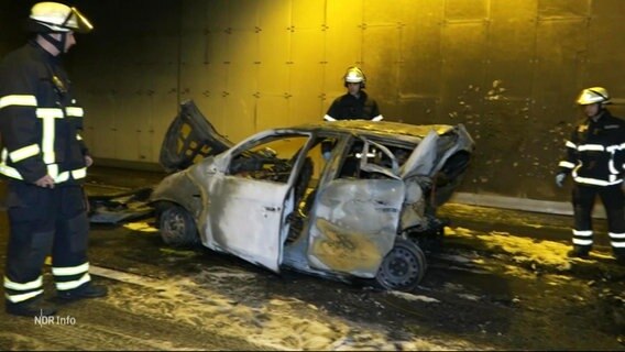 Mehrere Feuerwehrmenschen stehen um ein ausgebranntes Autowrack. © Screenshot 