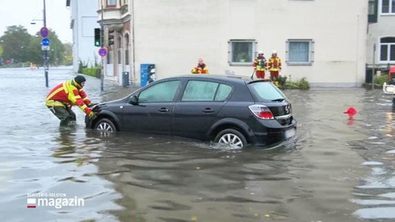 Feuerwehrleute versuchen einen PKW von einer überfluteten Straße zu bergen. © Screenshot 