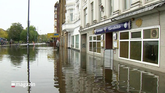 Wasser verdeckt einen Fußgängerbereich vor Geschäften. © Screenshot 