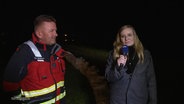 Anna-Lou Beckmann berichtet live in Wieck am Darß. Neben ihr steht ein Feuerwehrmann. © Screenshot 