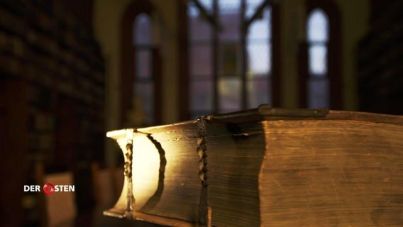 Ein altes Buch liegt in einer Bibliothek. © Screenshot 