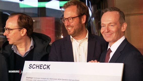 Bundesverkehrsminister Volker Wissing und zwei andere Männer halten einen Scheck in die Kamera und grinsen. © Screenshot 