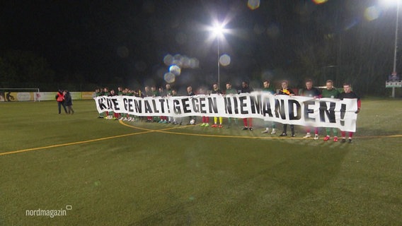 Menschen auf einem Fußballfeld mit einem Banner auf dem steht: Keine Gewalt gegen Niemanden. © Screenshot 