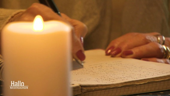 Eine Hand auf einem Block Papier und eine Kerze. © Screenshot 