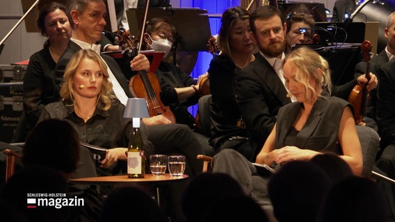 Das True-Crime Duo Leonie Bartsch und Linn Schütze tritt bei einer Live-Folge ihres Podcasts gemeinsam mit einem Orchester auf. © Screenshot 