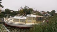 Ein vom Sturm aus dem Wasser gehobenes Motorboot liegt an Land. © Screenshot 