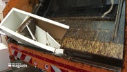 Ein weißes Regal wird in der Klappe eines Müllwagens zertquetscht. © Screenshot 