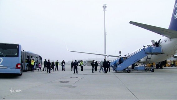Szene auf einem Rollfeld: Rechts im Bild ein Flugzeug mit einer angestellten Treppe, links ein Bus. Menschen steigen aus dem Bus aus und ins Flugzeug ein. © Screenshot 