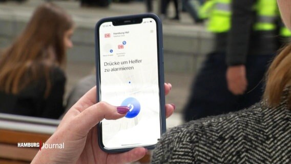 Eine Frau mit lackierten Fingernägeln hält ein Smartphone in der Hand mit der geöffneten Sicherheits App des Hamburger Hauptbahnhofes. © Screenshot 