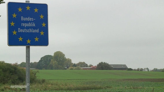 Das Schild "Bundesrepublik Deutschland" mit weißer Schrift auf blauem Grund und den Europa-Sternen darauf an einer Straße, im Hintergrund Felder. © Screenshot 