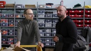Zwei Männer stehen vor einem Regal mit Plastikboxen: Marco Scheel, Gründer und Geschäftsführer von Nordwolle Rügen und sein Mitarbeiter Nicolai Zuicov. © Screenshot 