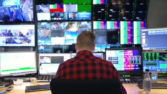 Ein Mann in einem karierten Hemd sitzt vor mehreren Bildschirmen. © Screenshot 
