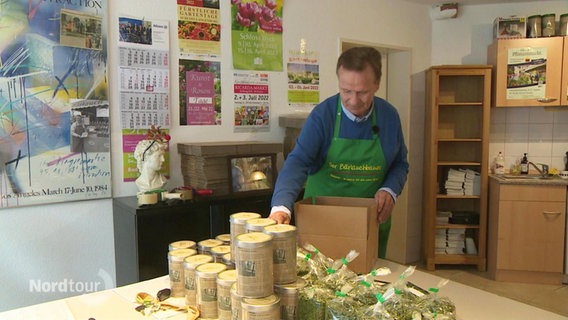 Ein Mann in grüner Schürze packt einige Beutel mit Produkten in einen kleineren Karton ein. © Screenshot 