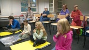 Mehrere Kinder sitzen auf gelben Matten vor ihren Großeltern bei einem Erste-Hilfe-Kurs. © Screenshot 