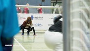Blick über das Spielfeld von Goalball. Eine Spielerin des FC St. Pauli hockt absprungbereit auf dem Boden vor ihrem Tor. Sie trägt eine Maske über den Augen. © Screenshot 