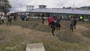 Nach einer Strumflut helfen viele Freiwillige bei Aufräumarbeiten an einer Promenade mit. © Screenshot 