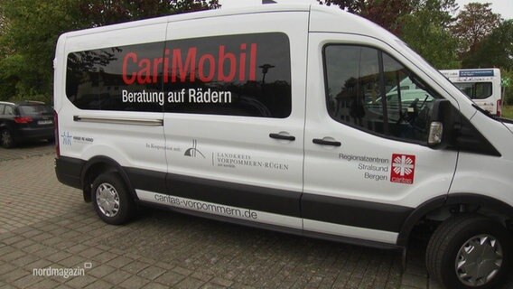 Ein weißer Kleinbus mit der Aufschrift "CariMobil" steht auf einem Parkplatz. © Screenshot 