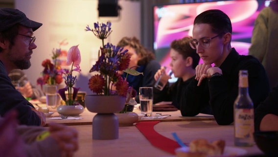 Eine Gruppe von Menschen treffen sich beim "Hummustopia" zu gesellschaftlichen Debatten. © Screenshot 