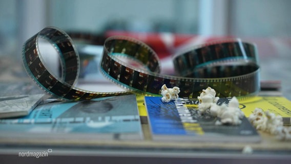 Eine Filmrolle, deren Film lose herumliegt und Popcorn-Hörner daneben. © Screenshot 