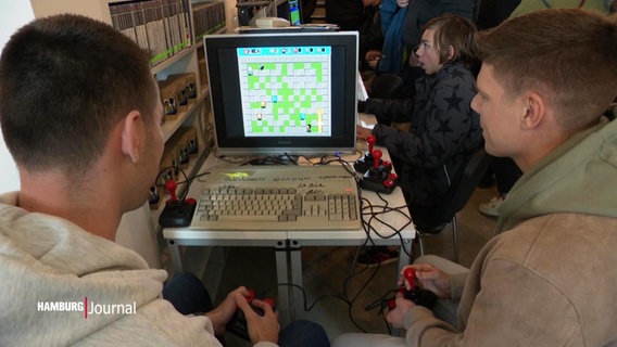 Menschen sitzen an einer alten Spielekonsole. © Screenshot 
