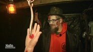 Ein Mann in einem Halloween-Kostüm. Im Vordergrund sieht man einen aufgespießte Hand mit Blut. © Screenshot 