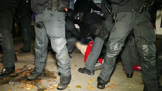 Die Beine von Menschen der Polizei und eine Person auf dem Boden, die festgenommen wird. © Screenshot 