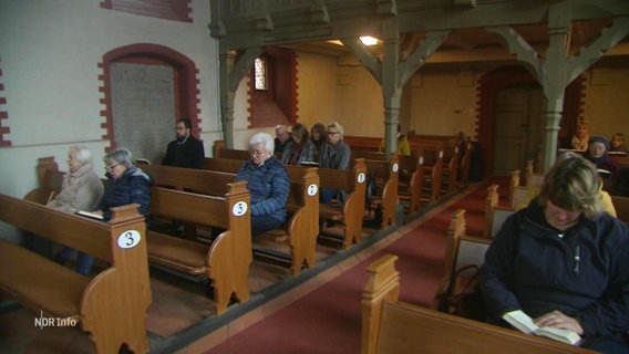 Menschen, die auf Kirchenbänken sitzen. © Screenshot 