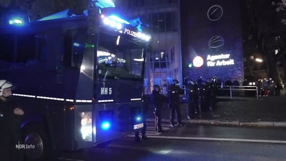 Ein Wasserwerfer der Polizei und Polizeibeamte mit Helmen und dunkler Uniform. © Screenshot 
