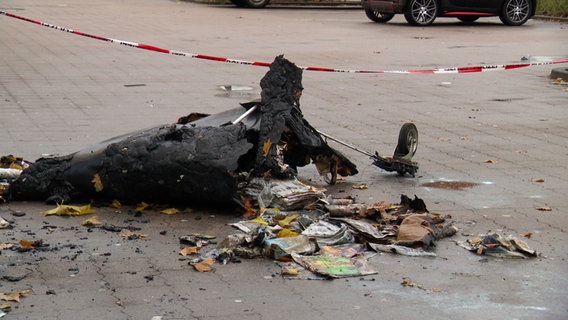 Verkohlte Überreste eines Abfallcontainers, aus dem Reste von Böllern und Feuerwerkskörpern fallen. Im Hintergrund Absperrband der Polizei. © Screenshot 
