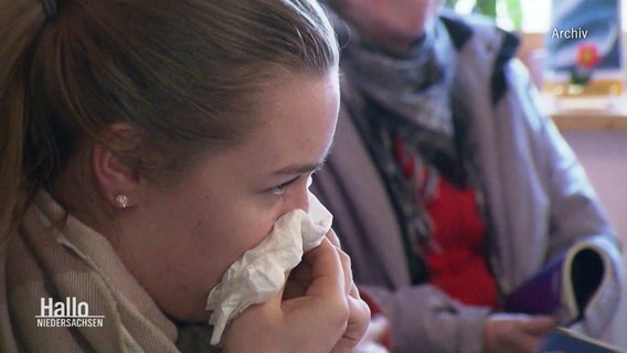Eine junge Frau putzt sich mit einem Taschentuch die Nase (Archivbild). © Screenshot 