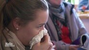 Eine junge Frau putzt sich mit einem Taschentuch die Nase (Archivbild). © Screenshot 