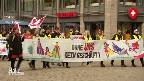 Szene bei dem Streik des Einzelhandels in Osnabrück: Streikende tragen ein langes Banner mit der Aufschrift "Ohne uns kein Geschäft!" © Screenshot 